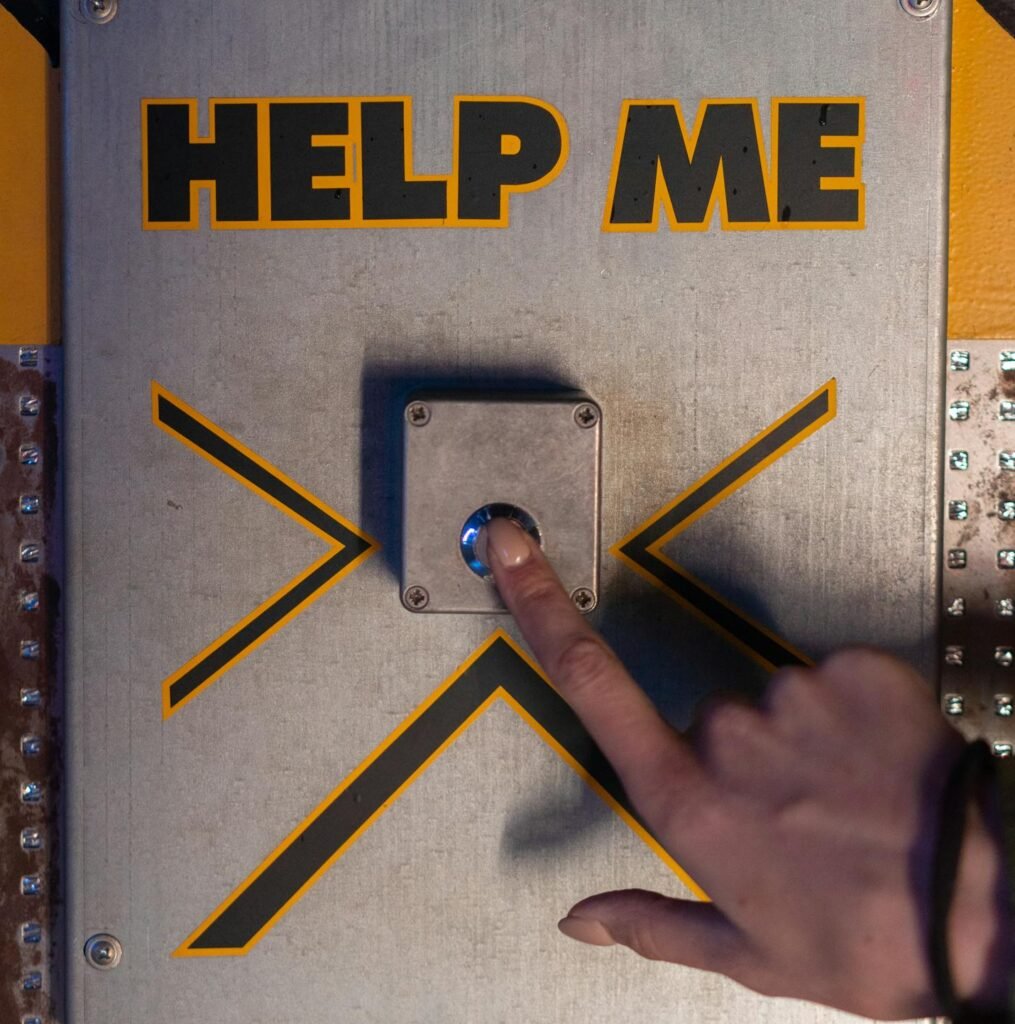 A hand presses an emergency 'help me' button on a metallic panel, evoking sci-fi themes.